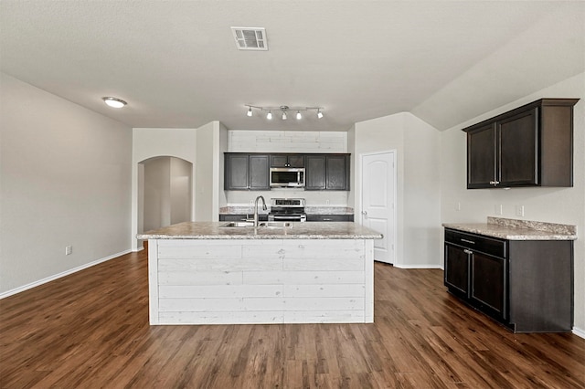 kitchen featuring dark wood-type flooring, a center island with sink, sink, light stone counters, and stainless steel appliances