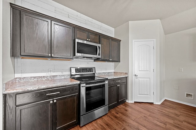 kitchen with light stone countertops, appliances with stainless steel finishes, tasteful backsplash, dark brown cabinetry, and dark hardwood / wood-style floors