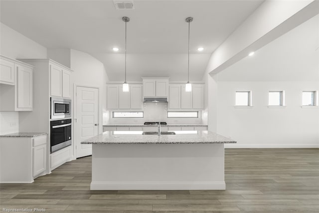 kitchen featuring white cabinets, appliances with stainless steel finishes, a center island with sink, and vaulted ceiling