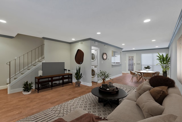 living room with ornamental molding, stacked washer and clothes dryer, and light wood-type flooring