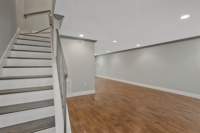 staircase with wood-type flooring and ornamental molding