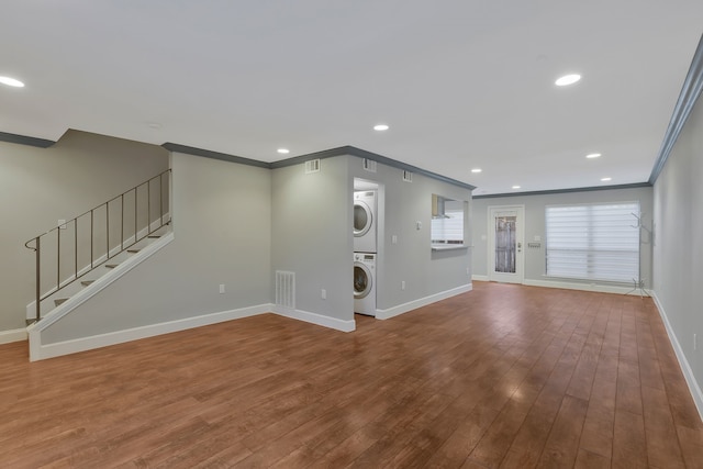 unfurnished living room with crown molding, stacked washer and dryer, and hardwood / wood-style flooring