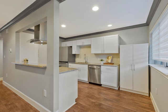 kitchen featuring appliances with stainless steel finishes, light wood-type flooring, sink, wall chimney range hood, and white cabinetry