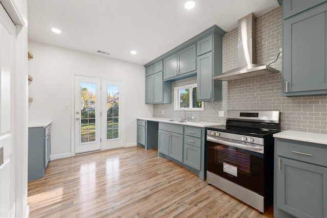 kitchen with decorative backsplash, stainless steel appliances, light hardwood / wood-style flooring, and wall chimney range hood