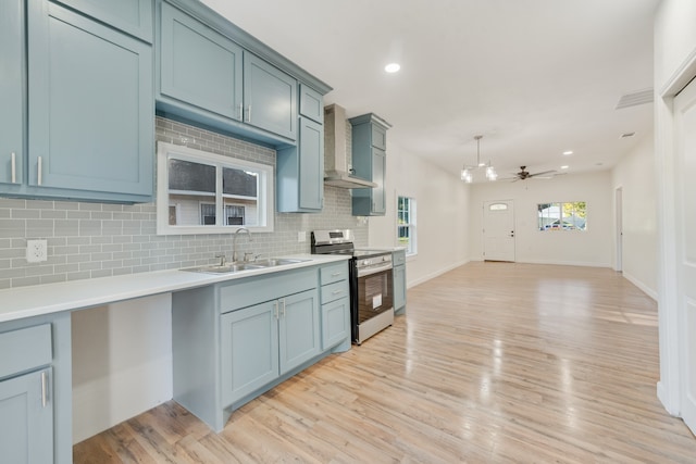 kitchen with wall chimney range hood, sink, light hardwood / wood-style flooring, ceiling fan, and stainless steel range