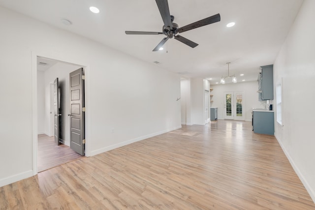 unfurnished living room featuring french doors, ceiling fan with notable chandelier, and light hardwood / wood-style floors