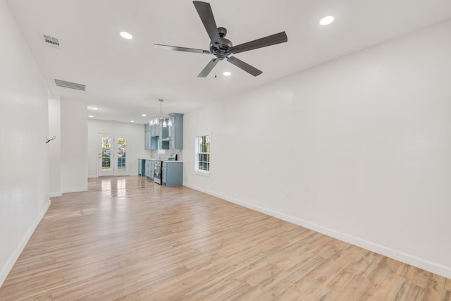 unfurnished living room featuring french doors, ceiling fan with notable chandelier, and light hardwood / wood-style flooring