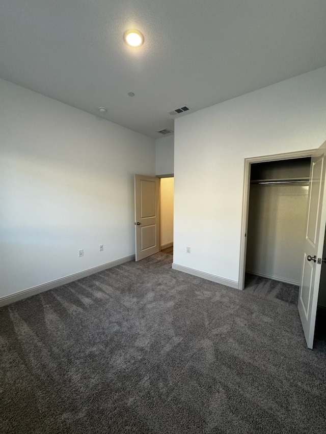 unfurnished bedroom with dark carpet and a closet