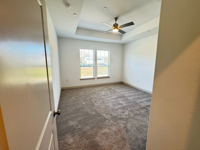 carpeted empty room featuring a raised ceiling and ceiling fan