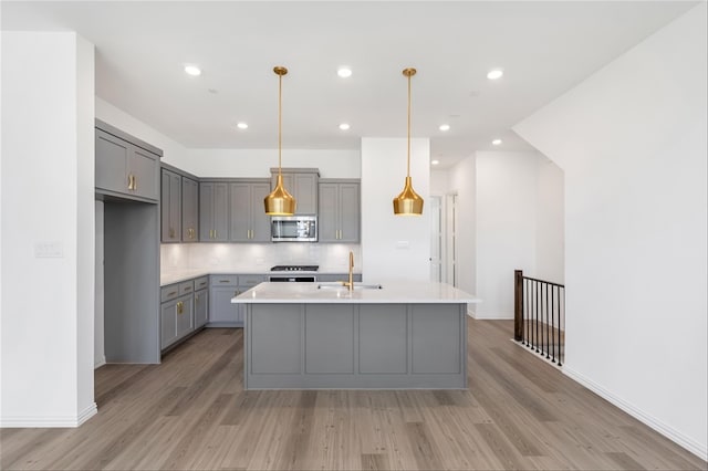 kitchen featuring appliances with stainless steel finishes, light hardwood / wood-style floors, a kitchen island with sink, and gray cabinetry