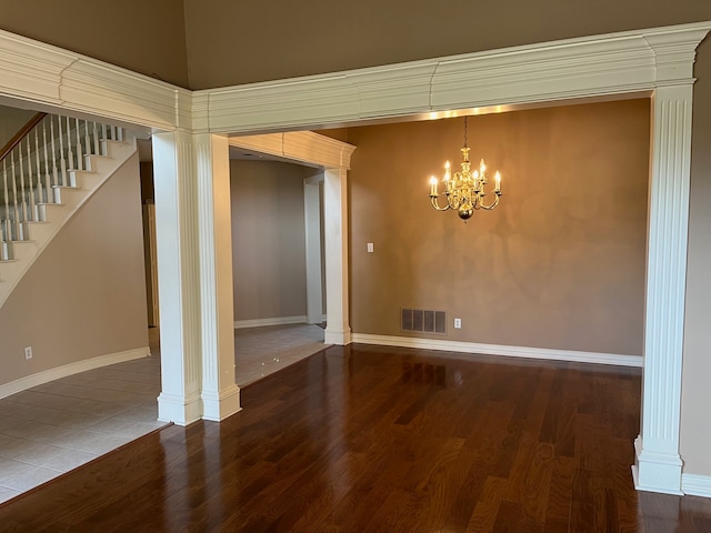 unfurnished room with decorative columns, wood-type flooring, and a notable chandelier