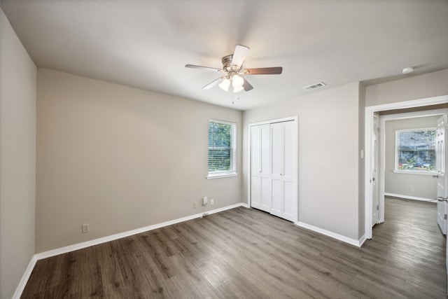 unfurnished bedroom with a closet, dark hardwood / wood-style floors, multiple windows, and ceiling fan