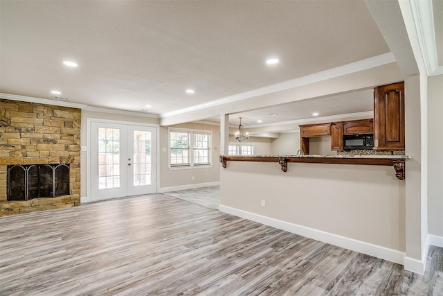 unfurnished living room with a stone fireplace, crown molding, french doors, and light wood-type flooring