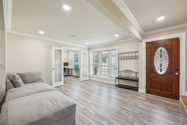 foyer with ornamental molding, light wood-type flooring, a textured ceiling, and french doors