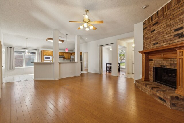 1306 Woodmont Dr, Allen, TX 75002 - unfurnished living room featuring plenty of natural light, a textured ceiling, ceiling fan, light wood-style flooring, and a fireplace