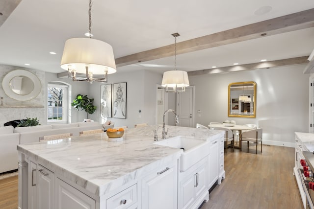 kitchen featuring a kitchen island with sink, sink, white cabinets, and hanging light fixtures