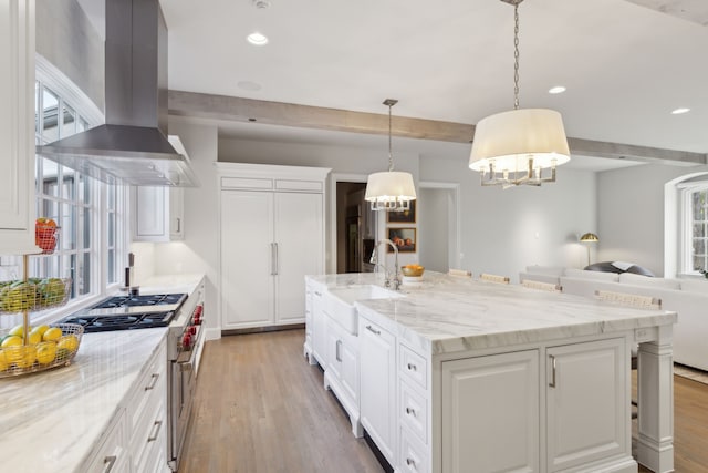 kitchen with island range hood, high end stainless steel range oven, decorative light fixtures, a center island with sink, and white cabinets