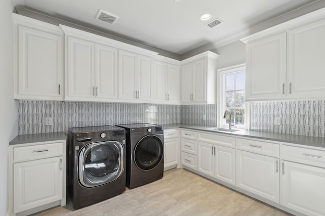 clothes washing area featuring cabinets, washing machine and dryer, light hardwood / wood-style floors, and sink