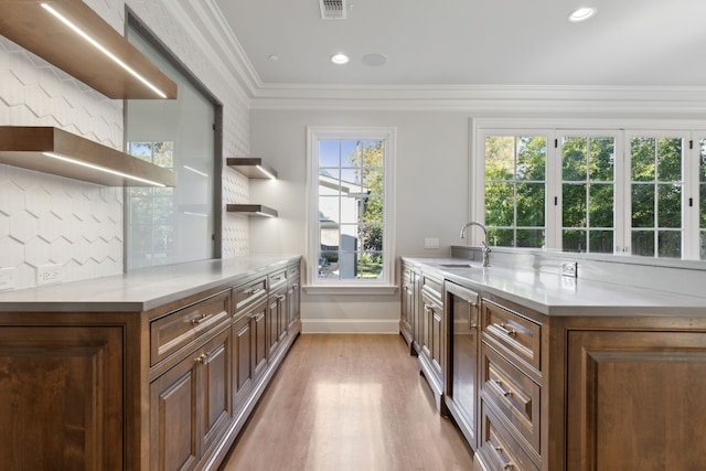 kitchen with sink, tasteful backsplash, light hardwood / wood-style floors, a center island with sink, and ornamental molding