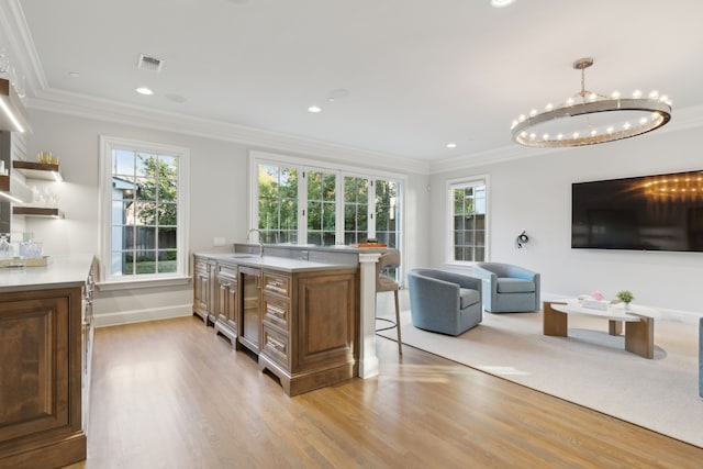 kitchen with a kitchen island with sink, hanging light fixtures, crown molding, and sink