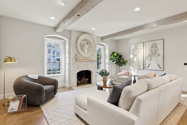 living room featuring beam ceiling, light wood-type flooring, and a brick fireplace