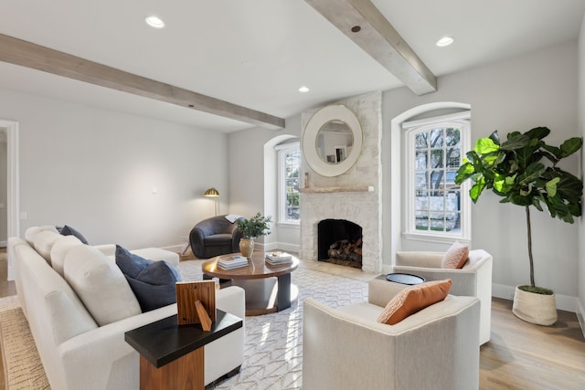 living room with beam ceiling, light hardwood / wood-style floors, a wealth of natural light, and a brick fireplace