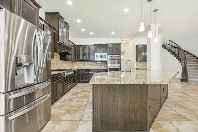 kitchen with dark brown cabinets, stainless steel appliances, hanging light fixtures, and an island with sink