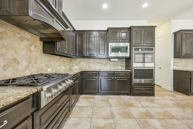 kitchen featuring backsplash, light stone counters, stainless steel appliances, and premium range hood