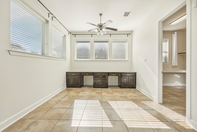 unfurnished office with ceiling fan, light tile patterned floors, and built in desk