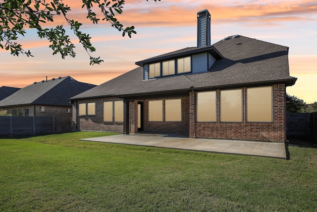 back house at dusk with a patio and a lawn