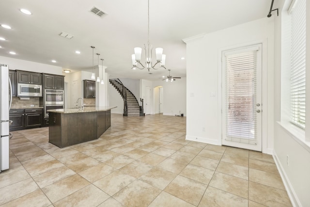 kitchen featuring stainless steel appliances, backsplash, pendant lighting, a center island with sink, and ceiling fan with notable chandelier