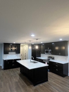 kitchen featuring dark wood-type flooring, sink, hanging light fixtures, an island with sink, and stainless steel appliances