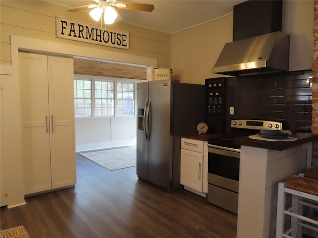 kitchen featuring a kitchen bar, appliances with stainless steel finishes, dark hardwood / wood-style flooring, wall chimney range hood, and white cabinetry