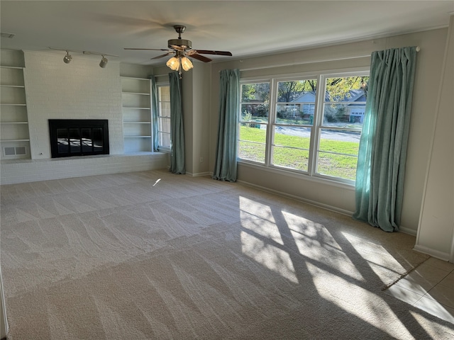 unfurnished living room featuring light carpet, built in features, ceiling fan, and a brick fireplace