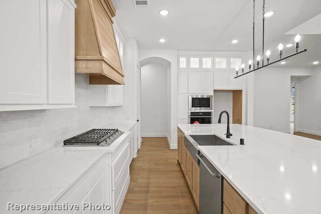 kitchen with hanging light fixtures, custom range hood, appliances with stainless steel finishes, light stone counters, and white cabinetry