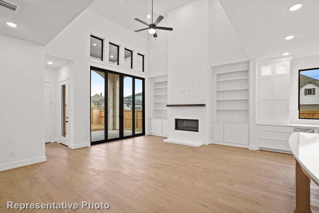 unfurnished living room with a high ceiling, ceiling fan, built in shelves, light hardwood / wood-style floors, and a large fireplace