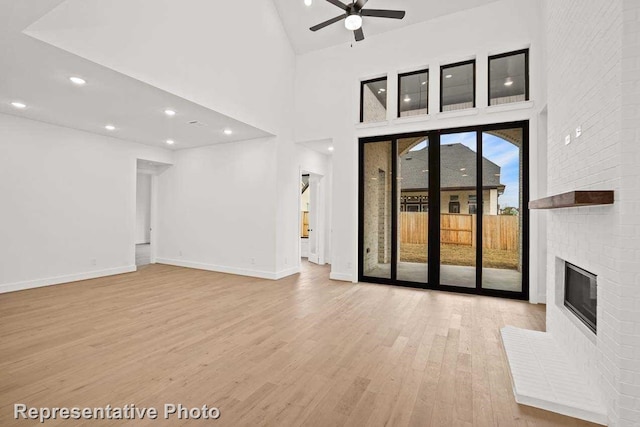 unfurnished living room with ceiling fan, light wood-type flooring, a high ceiling, and a brick fireplace