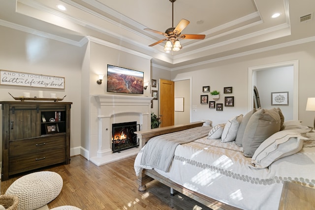 bedroom featuring hardwood / wood-style flooring, ceiling fan, ornamental molding, and a tray ceiling