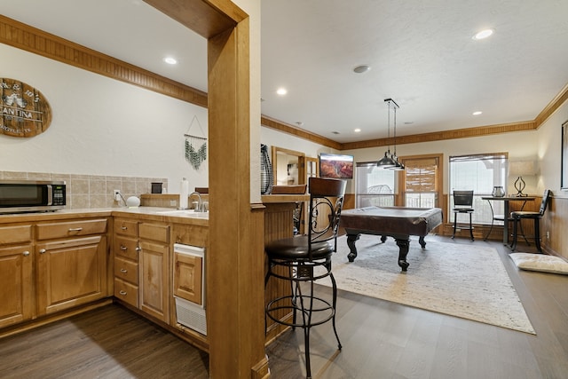 kitchen with dark wood-type flooring, crown molding, pendant lighting, a breakfast bar, and pool table