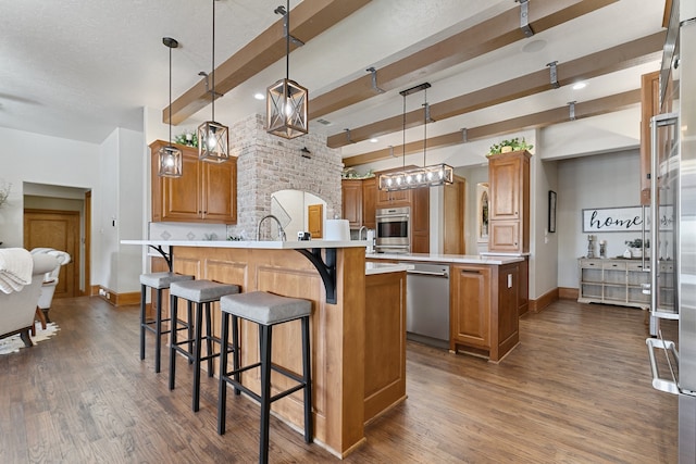 kitchen with beam ceiling, dark wood-type flooring, pendant lighting, a kitchen island, and appliances with stainless steel finishes