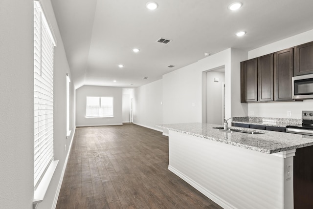 kitchen featuring stainless steel appliances, sink, light stone counters, a center island with sink, and dark brown cabinets