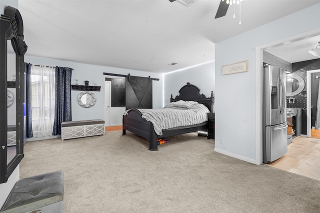 bedroom with carpet flooring, ceiling fan, a barn door, and stainless steel fridge with ice dispenser