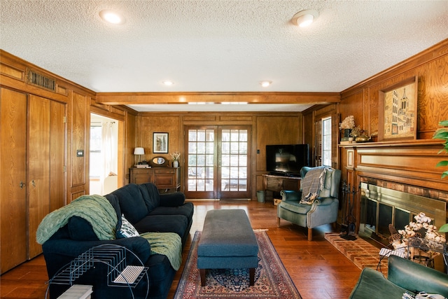 living room featuring a textured ceiling, dark hardwood / wood-style flooring, a brick fireplace, and wood walls