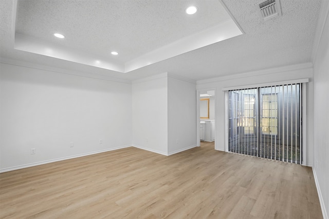 spare room featuring a tray ceiling, ornamental molding, a textured ceiling, and light wood-type flooring