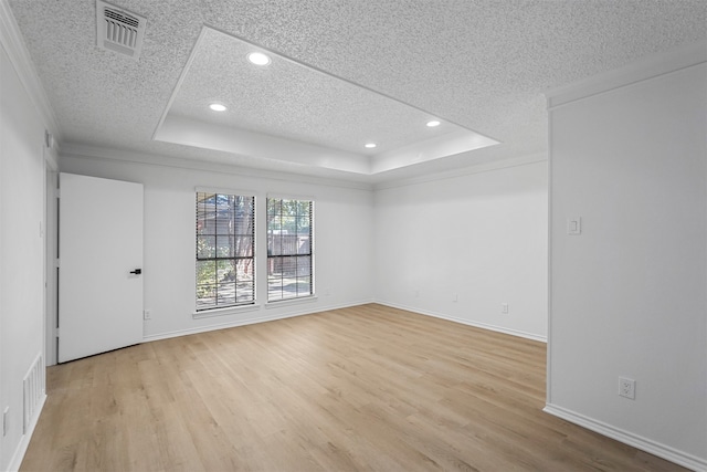 empty room with light hardwood / wood-style floors, a raised ceiling, and a textured ceiling