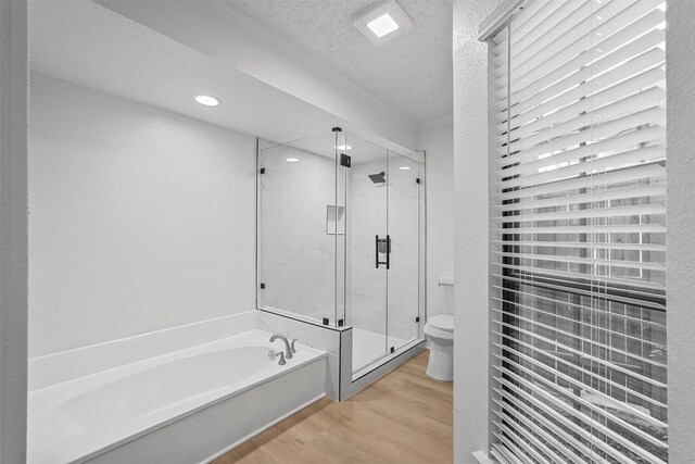 bathroom featuring a textured ceiling, toilet, shower with separate bathtub, and hardwood / wood-style flooring