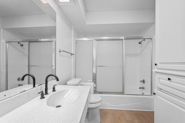 full bathroom with vanity, shower / bath combination with glass door, toilet, a textured ceiling, and wood-type flooring