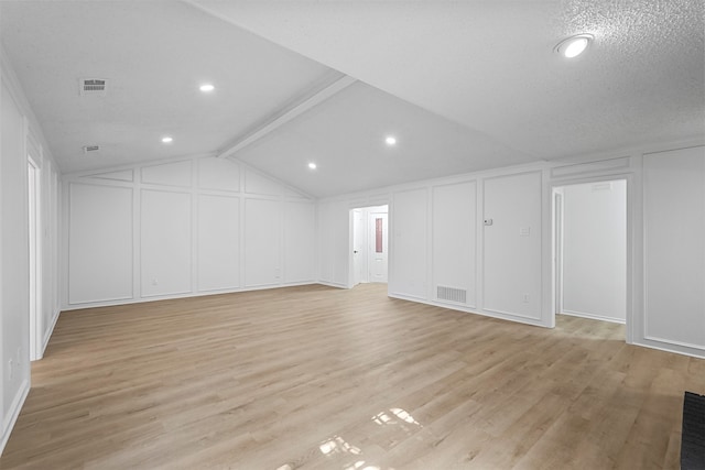 additional living space with lofted ceiling with beams, a textured ceiling, and light hardwood / wood-style floors