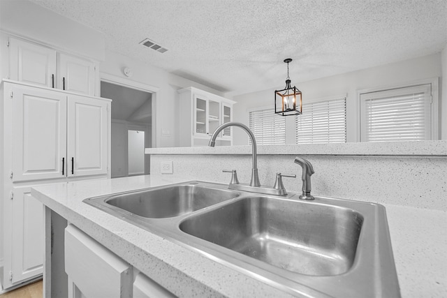 kitchen with white cabinets, a textured ceiling, hanging light fixtures, and sink