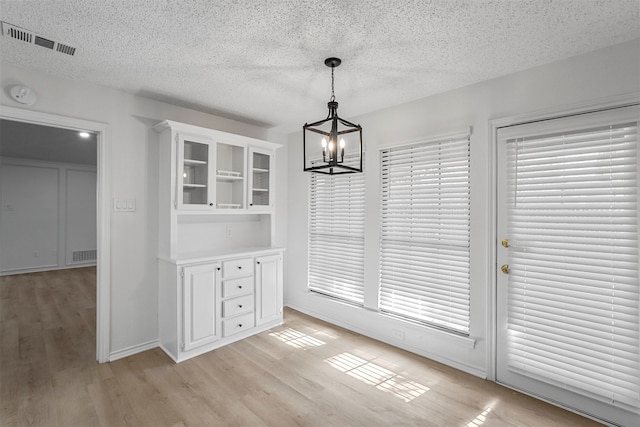 unfurnished dining area featuring a chandelier, a textured ceiling, and light hardwood / wood-style flooring